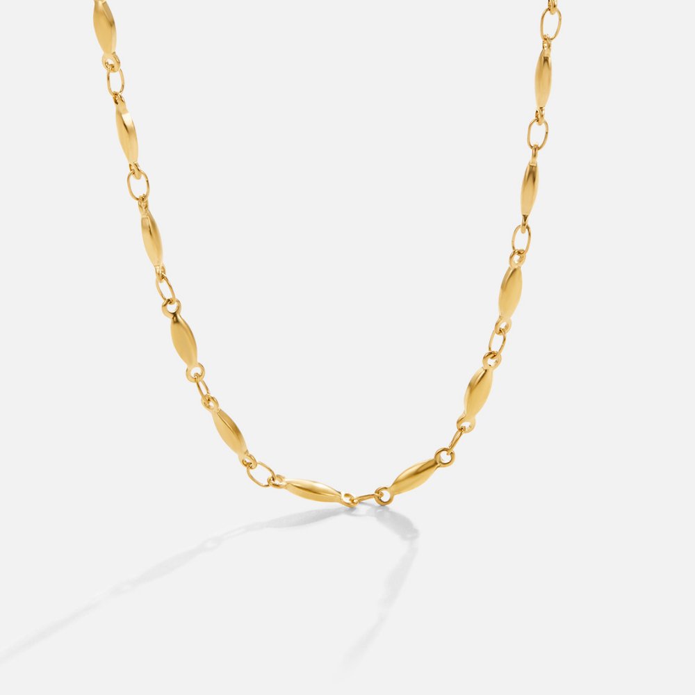 Alea Chain Necklace, gold chain necklace laid in a loose curve on white, with its shadow