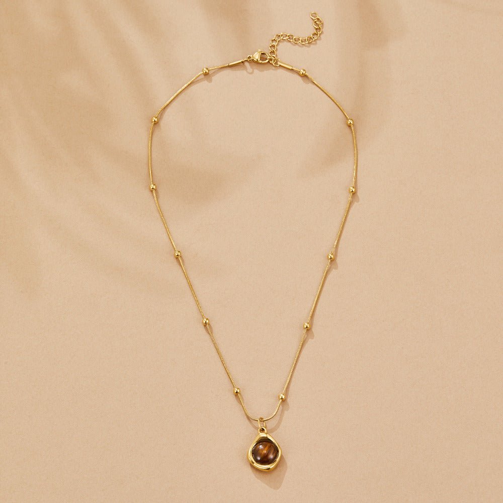Amber Stone Pendant Necklace, laid flat on beige fabric, gold chain with a brown stone pendant