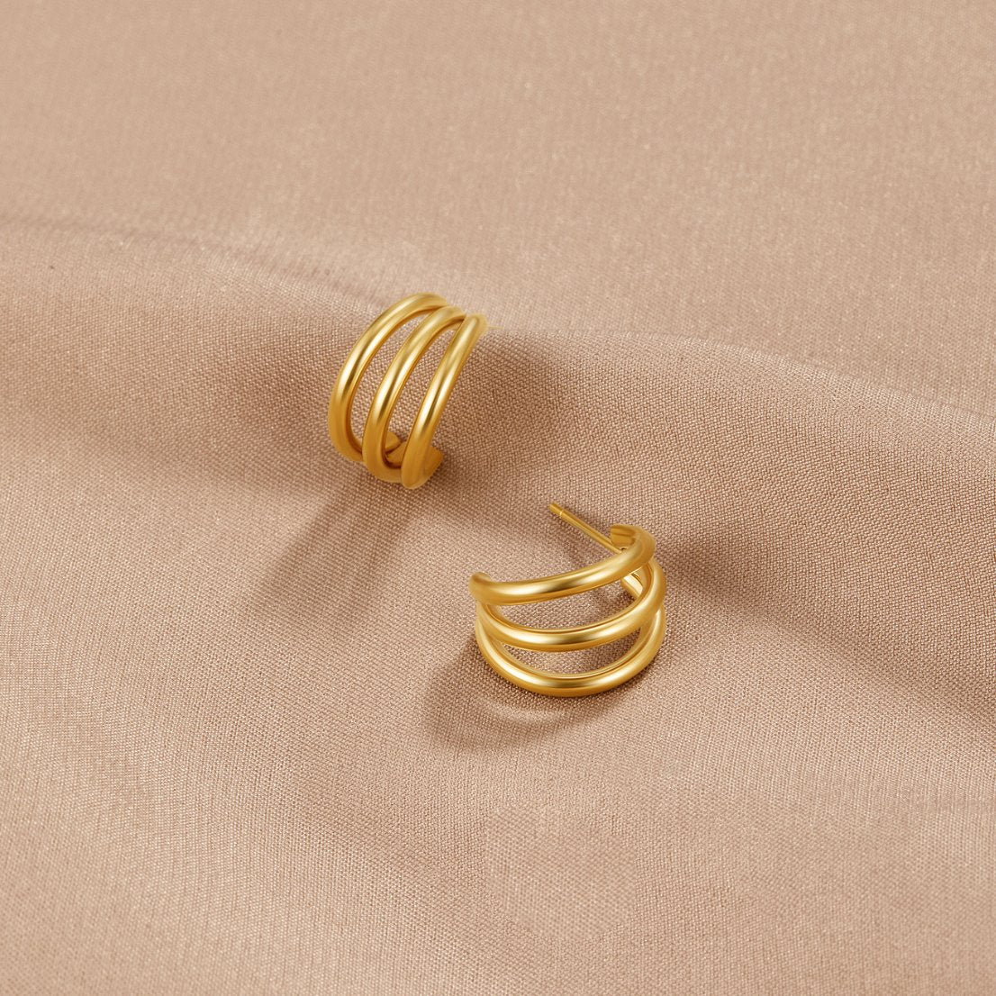 Anaya Triple Gold Hoop Earrings, two gold triple-band hoop earrings lying on beige fabric