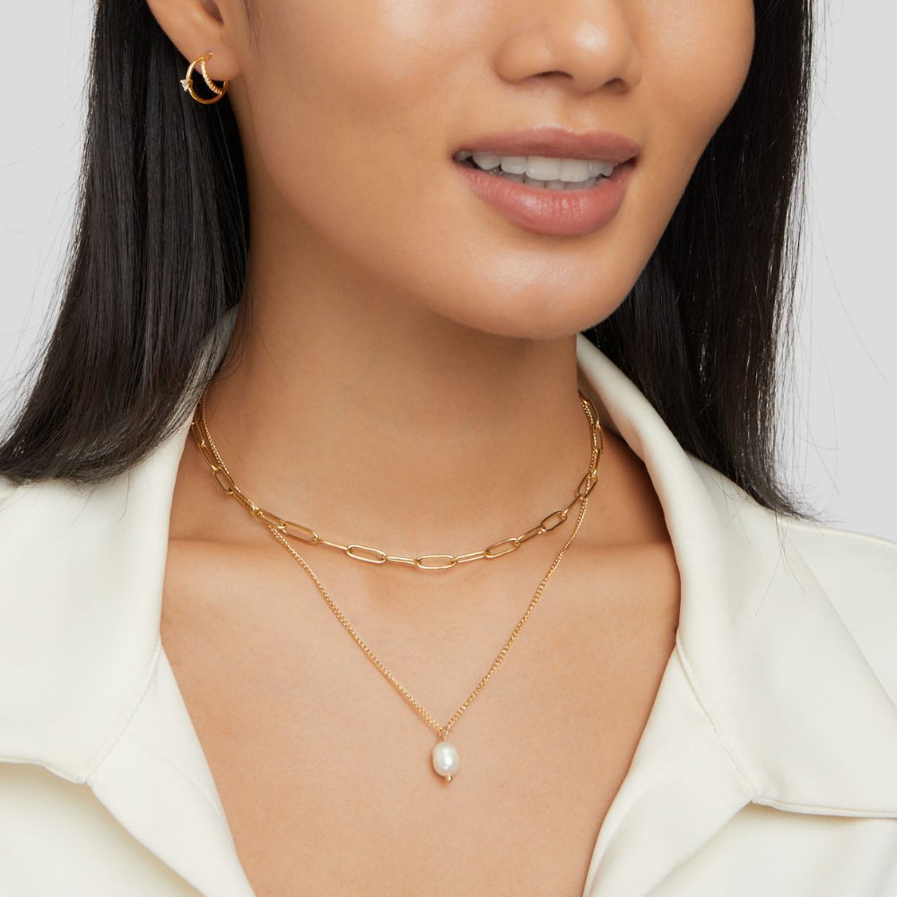 Angela Pearl Gold Necklace, worn on a model with a gold hoop earring visible