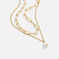 Angela Pearl Gold Necklace, layered gold chains on a plain background, with a pearl pendant
