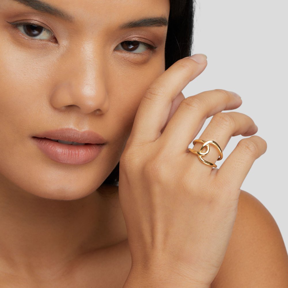 Astrid Gold Ring, worn on a hand near a model's face, gold interlocking loops