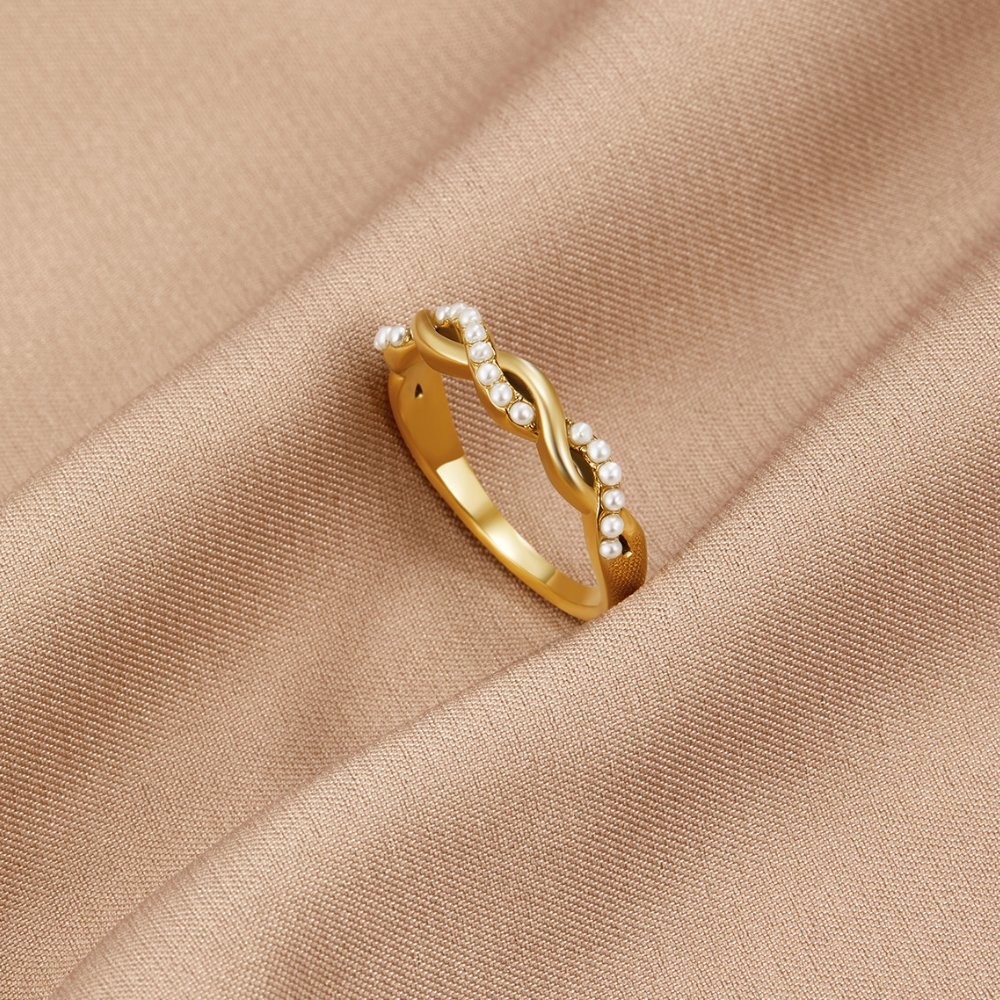 Bella Twist Pearl Ring, lying on draped beige fabric, gold twisted band with small pearls