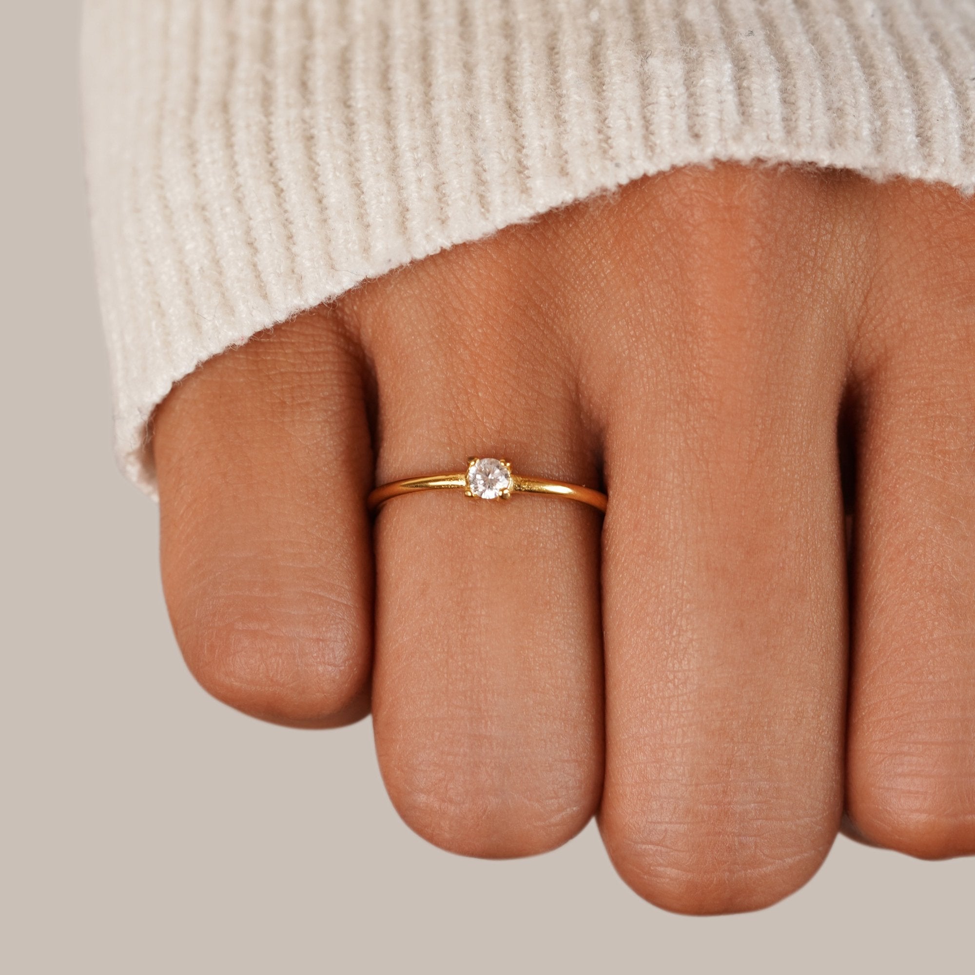 Birthstone 18K Gold Rings, worn on a finger with a cream knit sleeve, small round stone
