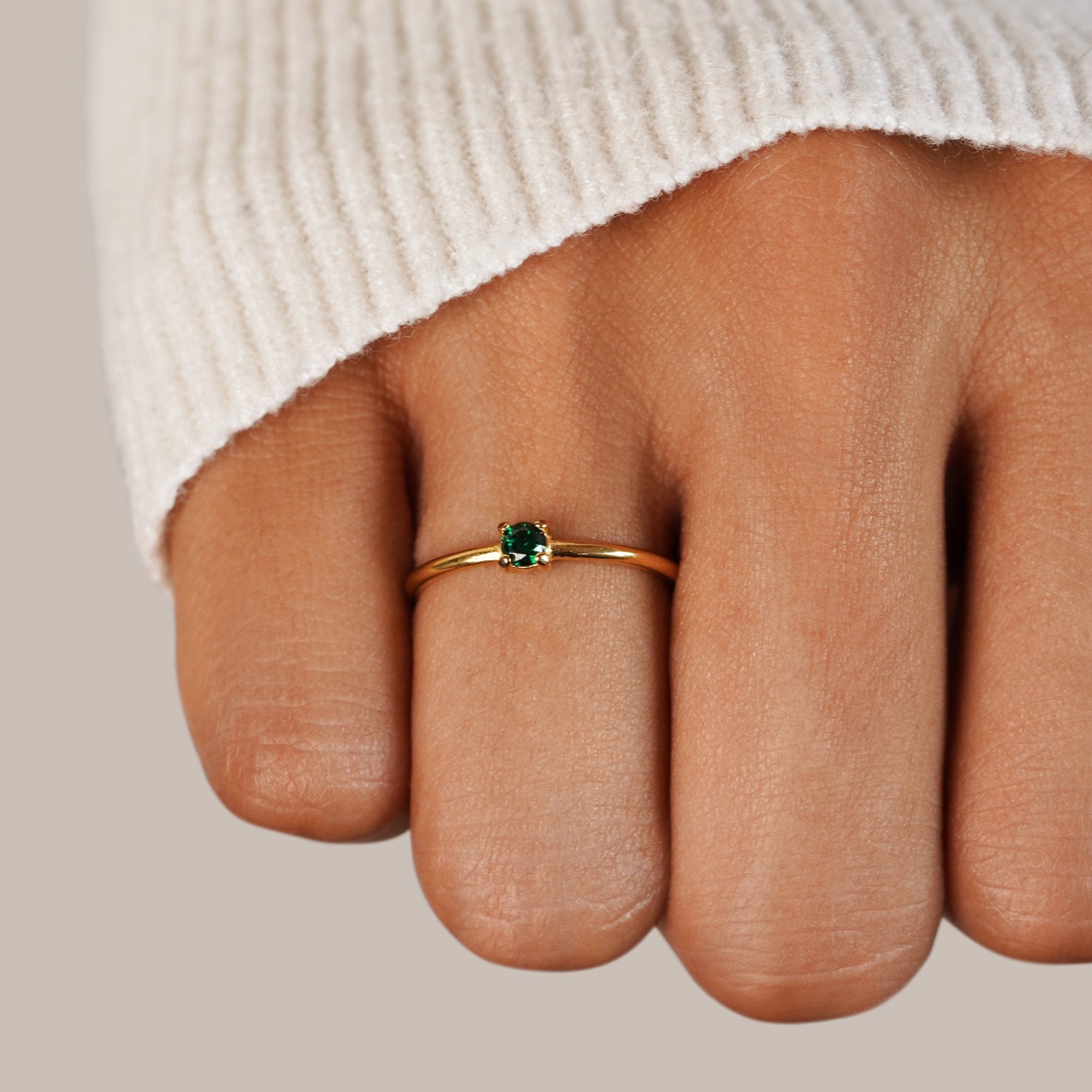 Birthstone 18K Gold Rings, worn on a hand in a cream knit sleeve, small green stone