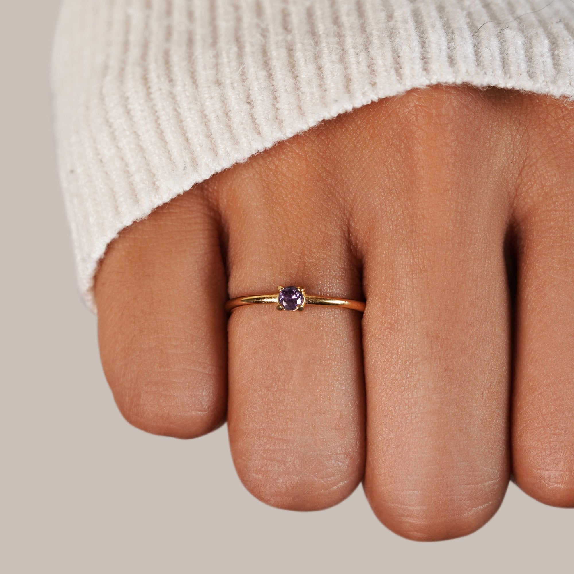 Birthstone 18K Gold Rings, worn on a finger with a cream knit sleeve, purple stone