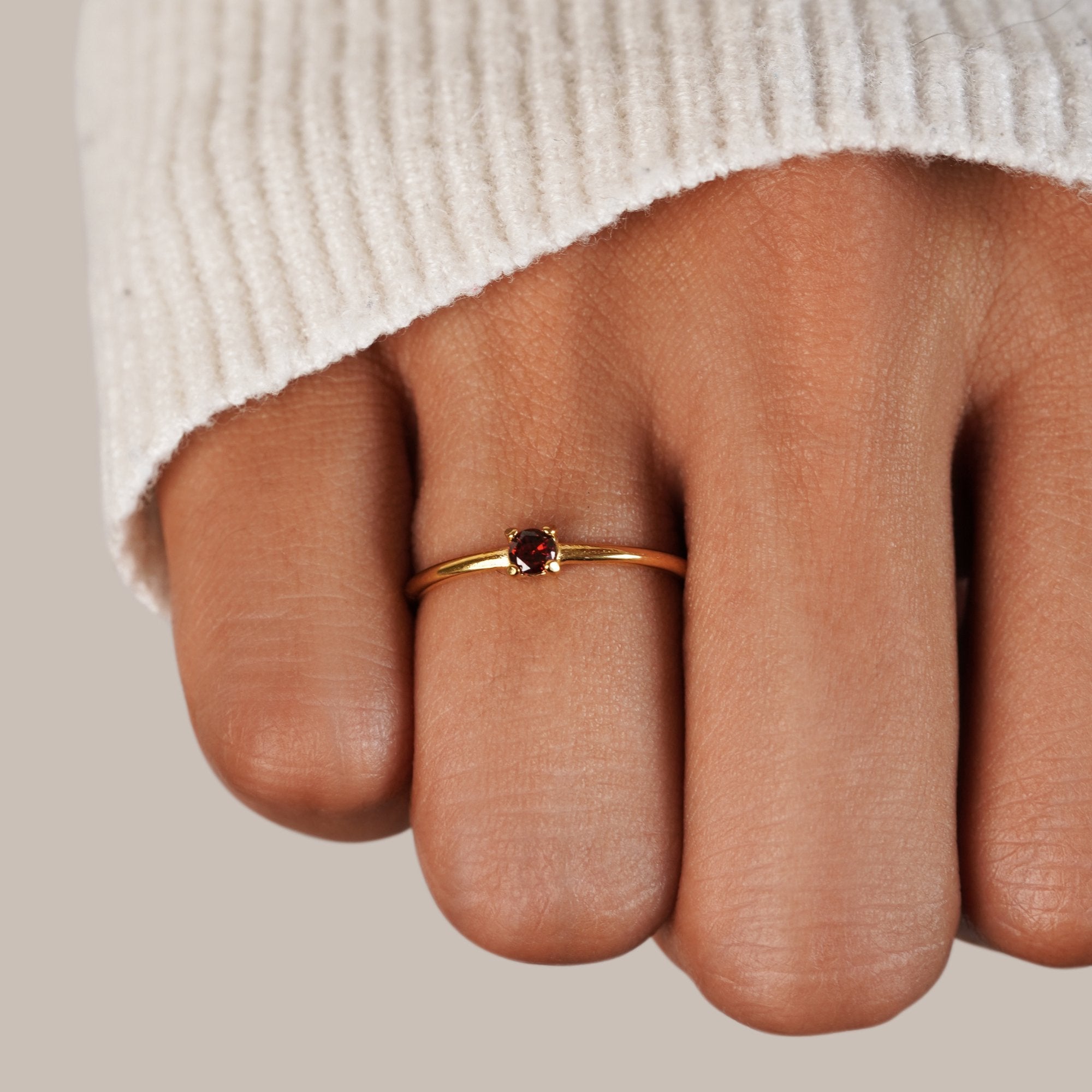 Birthstone 18K Gold Rings, worn on a finger in a cream knit sleeve, red stone