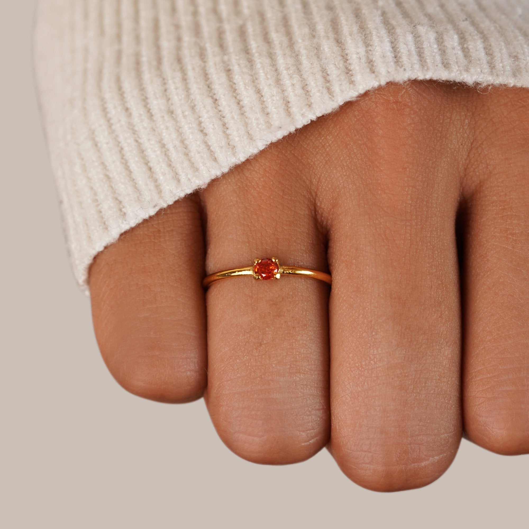 Birthstone 18K Gold Rings, worn on a finger with a cream knit sleeve, red stone