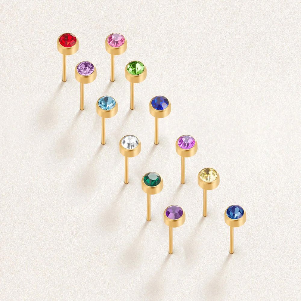 Birthstone Stud Earrings, twelve gold stud earrings with coloured gems, laid out in a diagonal