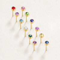 Birthstone Stud Earrings, twelve gold stud earrings with coloured gems, laid out in a diagonal