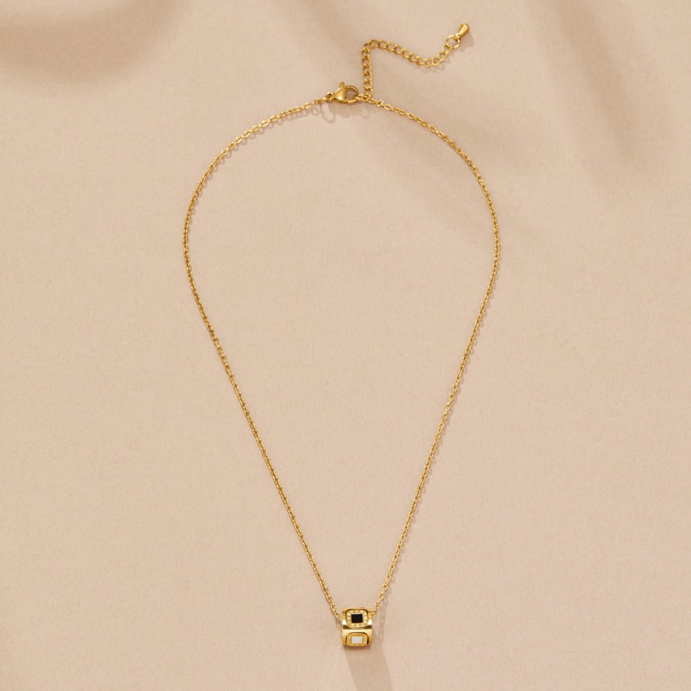 Black Agate Cube Pendant Necklace, laid flat on beige fabric, gold chain with cube pendant