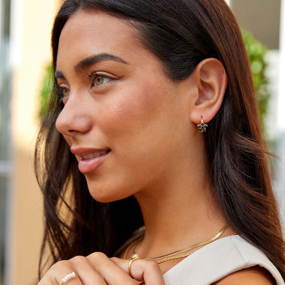Black Crystal Flower Hoop Earrings, worn on an ear with a gold layered necklace and rings