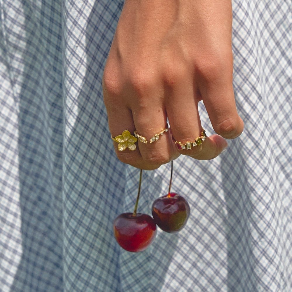 Blooming Gold Flower Ring, worn on a hand holding cherries over a plaid dress