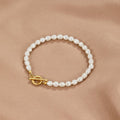 Cara Pearl Link Bracelet, laid flat on beige satin with white pearls and gold T-bar clasp