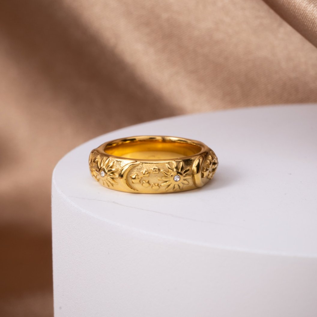 Celestial Gold Ring, standing on a white pedestal, gold band with raised sun and moon carvings