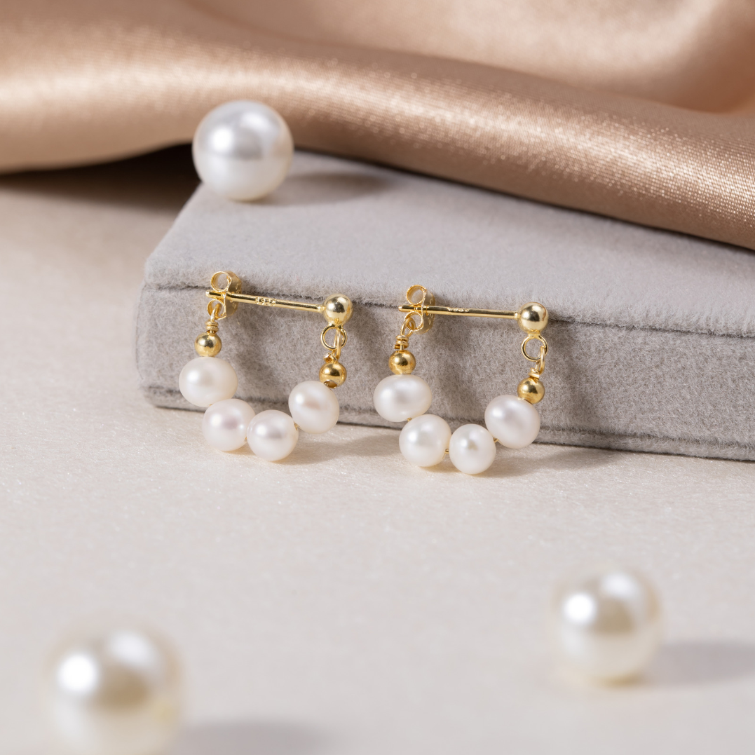 Celine Pearl Hoop Earrings, a pair of gold earrings with pearl clusters on a grey velvet box