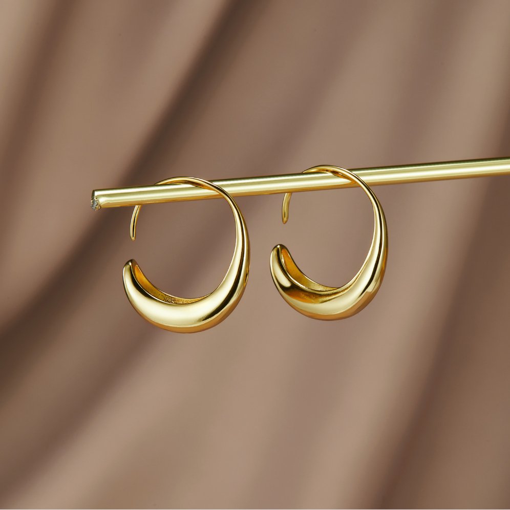 Classic Drop Hoop Earrings, pair of gold crescent hoop earrings hanging from a gold rod against brown fabric