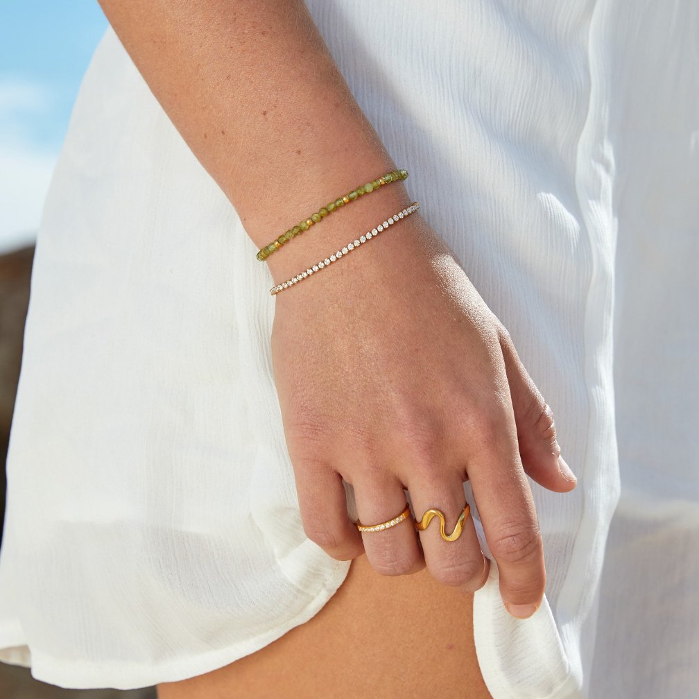 Cordelia Gold Tennis Bracelet, worn on a wrist with a green beaded bracelet and gold rings
