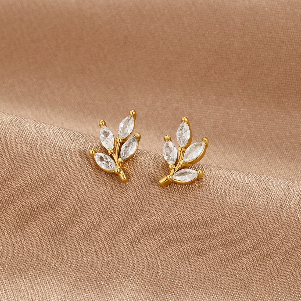 Crystal Leaf Stud Earrings, a pair of gold leaf studs with clear marquise stones on beige fabric