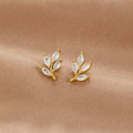 Crystal Leaf Stud Earrings, a pair of gold leaf studs with clear marquise stones on beige fabric
