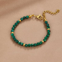 Emerald Green Beaded Bracelet, laid flat on a beige fabric, green banded beads with gold spacers