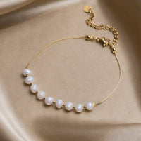 Eva Freshwater Pearl Bracelet, laid flat on cream satin with a row of white pearls and gold chain