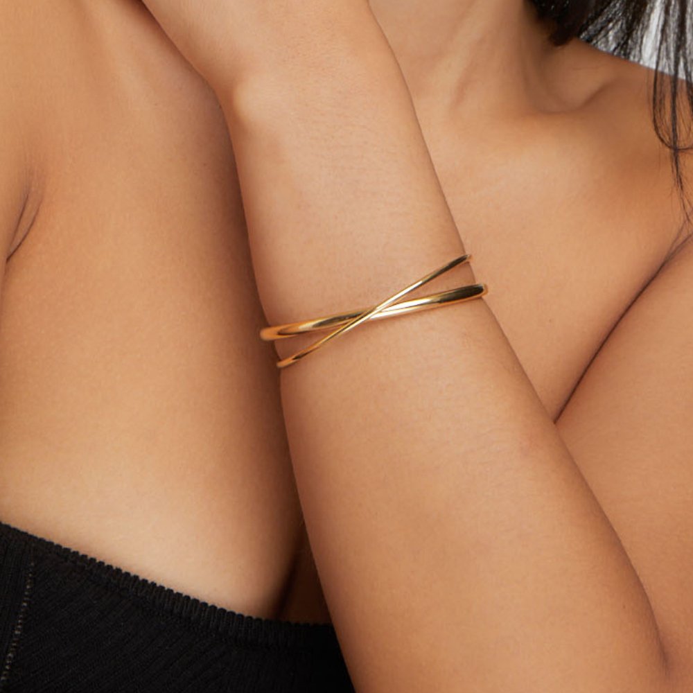 Eva Gold Twist Bracelet, worn on a bare arm, crossed gold bands at the wrist