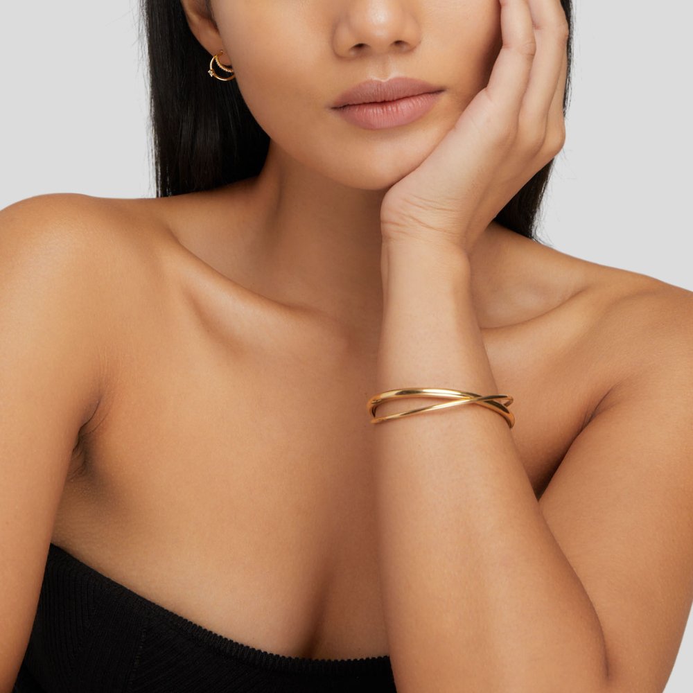 Eva Gold Twist Bracelet, worn on a wrist resting against a cheek, with a gold hoop earring
