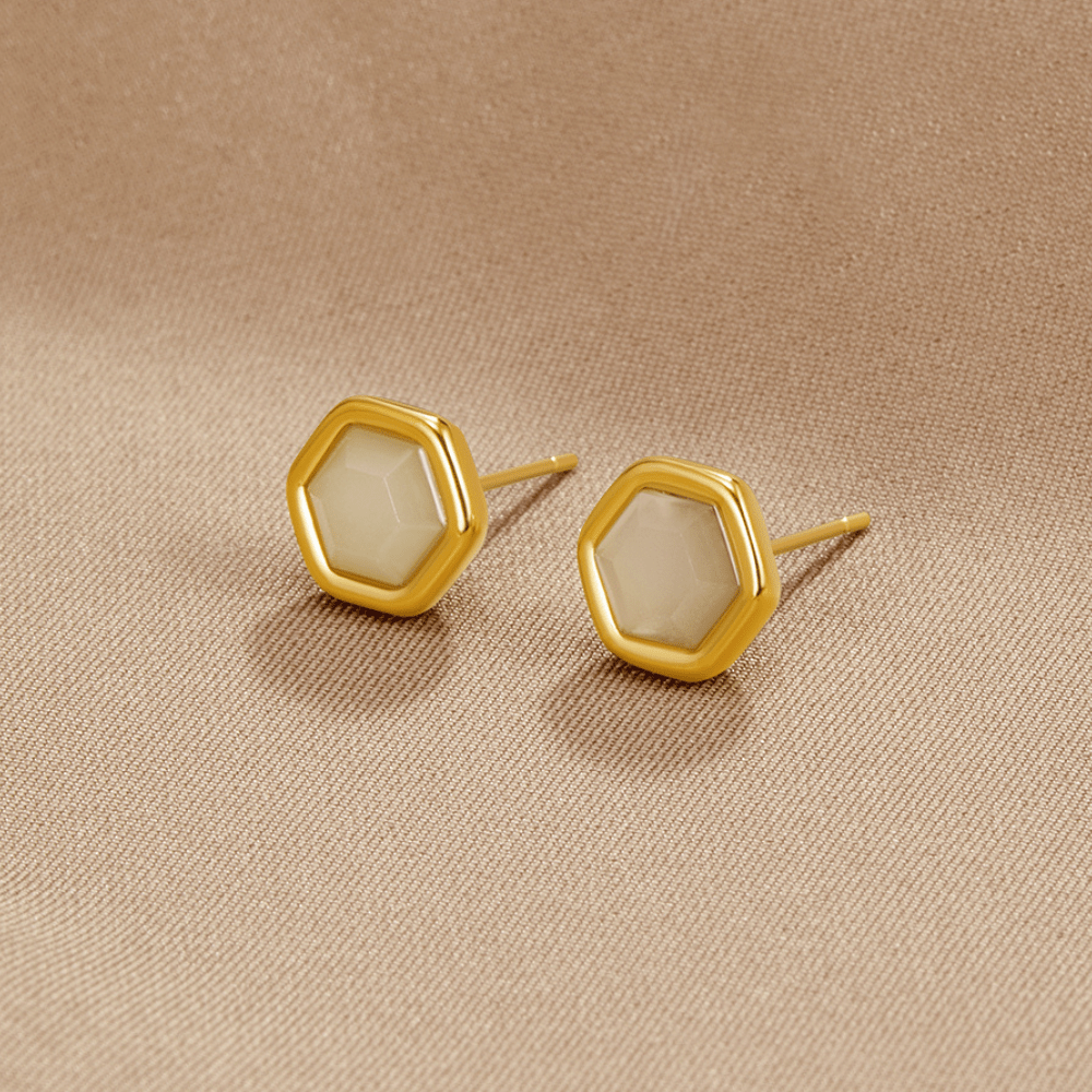Eva Moonstone Stud Earrings, a pair of hexagonal gold studs lying on beige fabric, pale stones