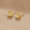Eva Moonstone Stud Earrings, a pair of hexagonal gold studs lying on beige fabric, pale stones