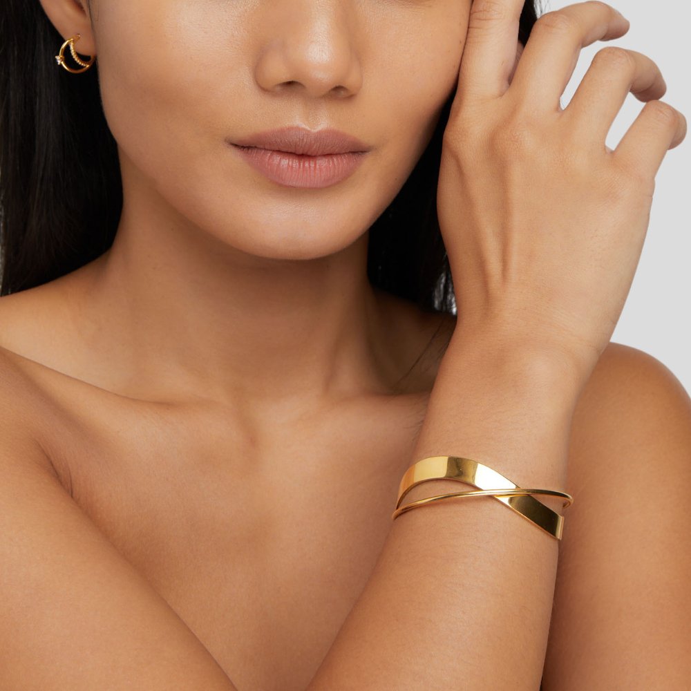 Eve Gold Bangle, worn on a wrist with a hand raised to the face, polished gold