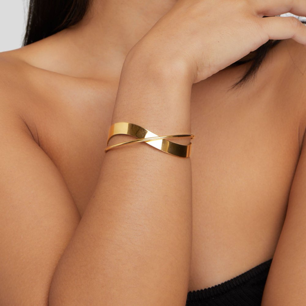 Eve Gold Bangle, worn on a wrist, crossed gold cuff with a twisted band