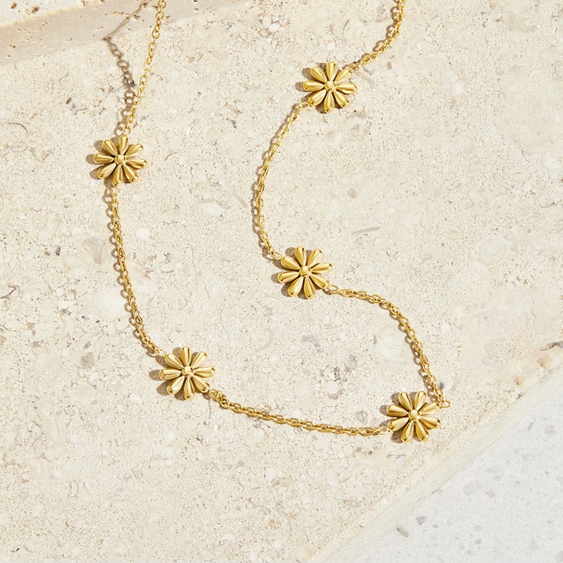 Flower Power 18K Gold Necklace, gold chain necklace with five flower motifs, laid on pale stone