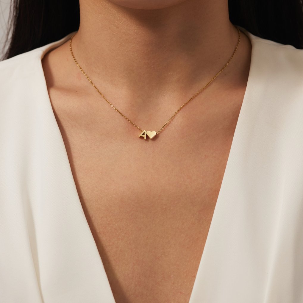 Forever Love & Letter Gold Necklace, worn on a neck with a white V-neck top, gold letter A and heart