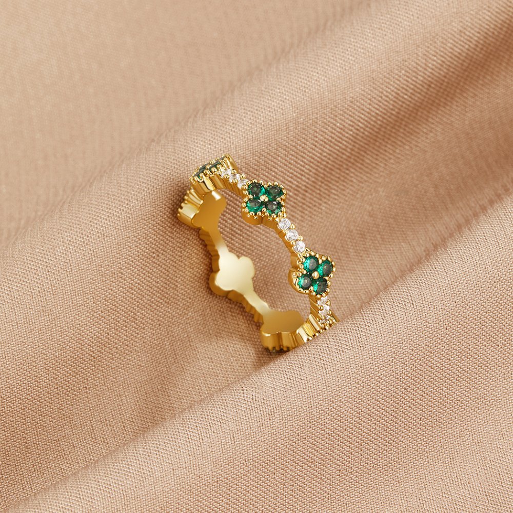 Four Leaf Clover Crystal Ring, gold band with green clover motifs on beige fabric