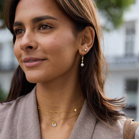 Free Sofia Pearl Stud Earrings, worn on a woman with gold drop earrings and layered necklaces