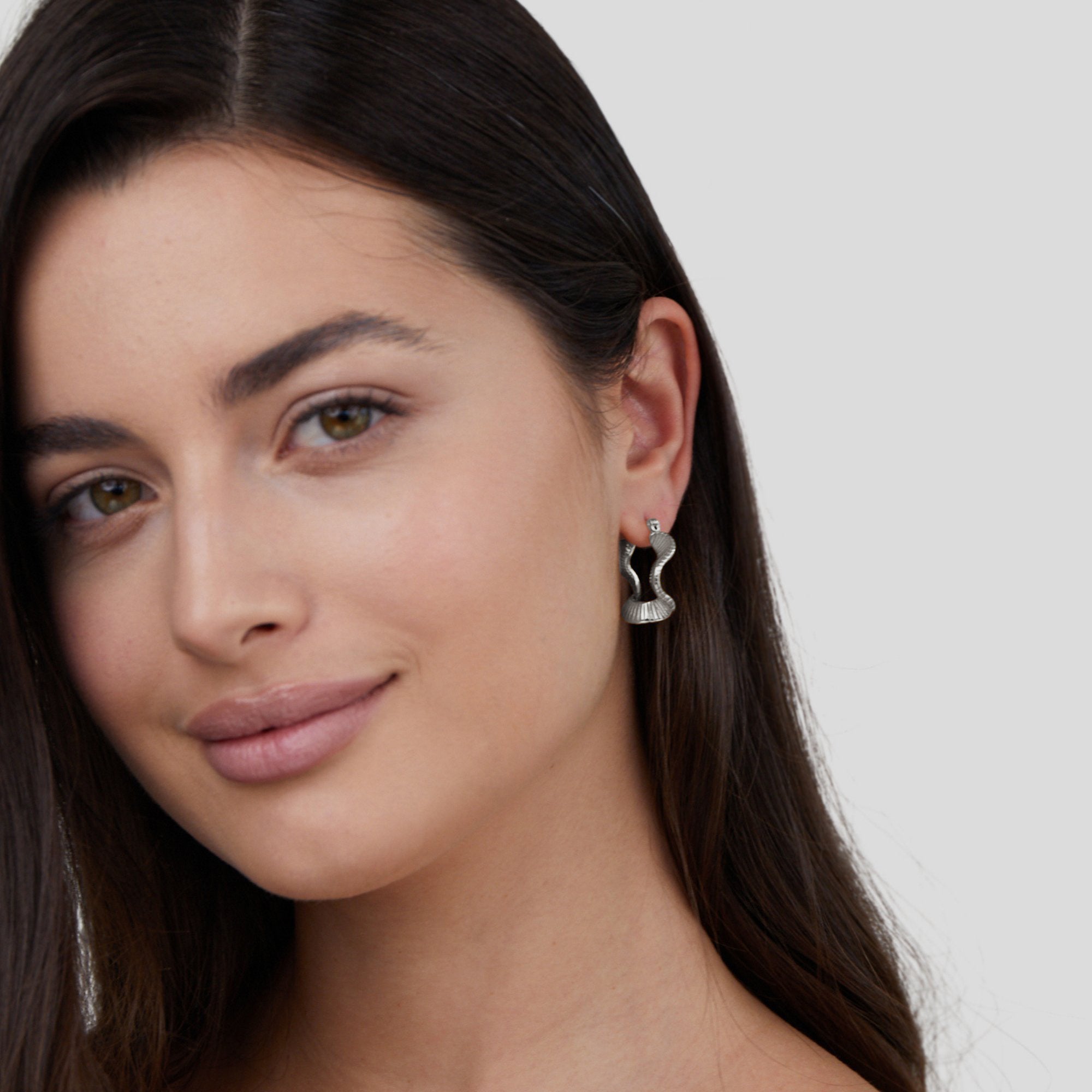 Geometric Wave Silver Hoop Earrings, worn on an ear by a woman with long dark hair