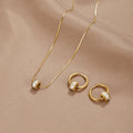 Gigi 18K Gold Set, flat-laid on a beige satin cloth, necklace and two hoop earrings