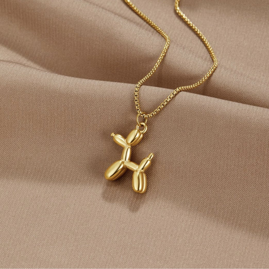 Gold Balloon Animal Necklace, gold balloon-dog pendant on a box chain, laid on satin