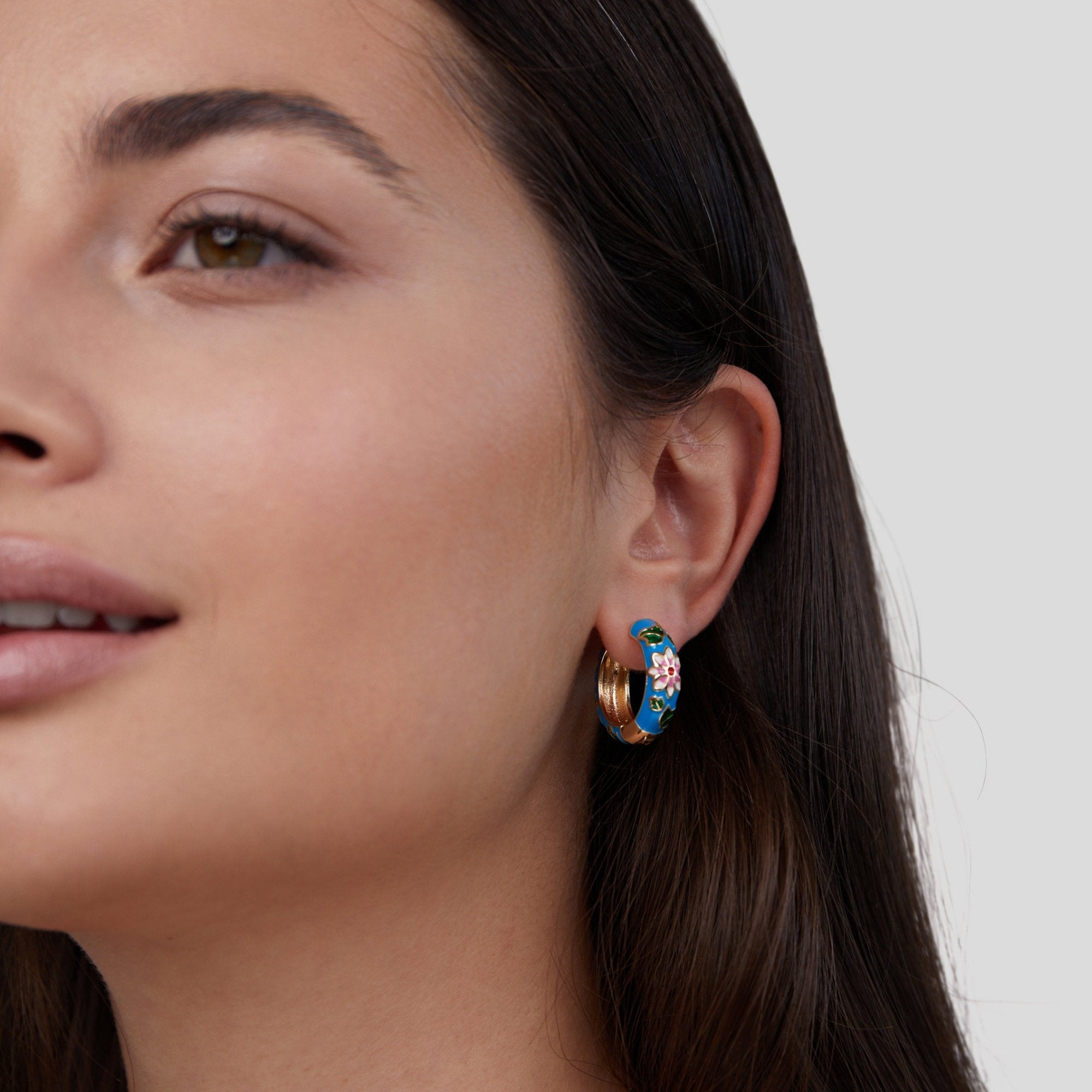 Gold Hoop Flower Earrings, worn on an ear, blue enamel with a pink flower and gold edge