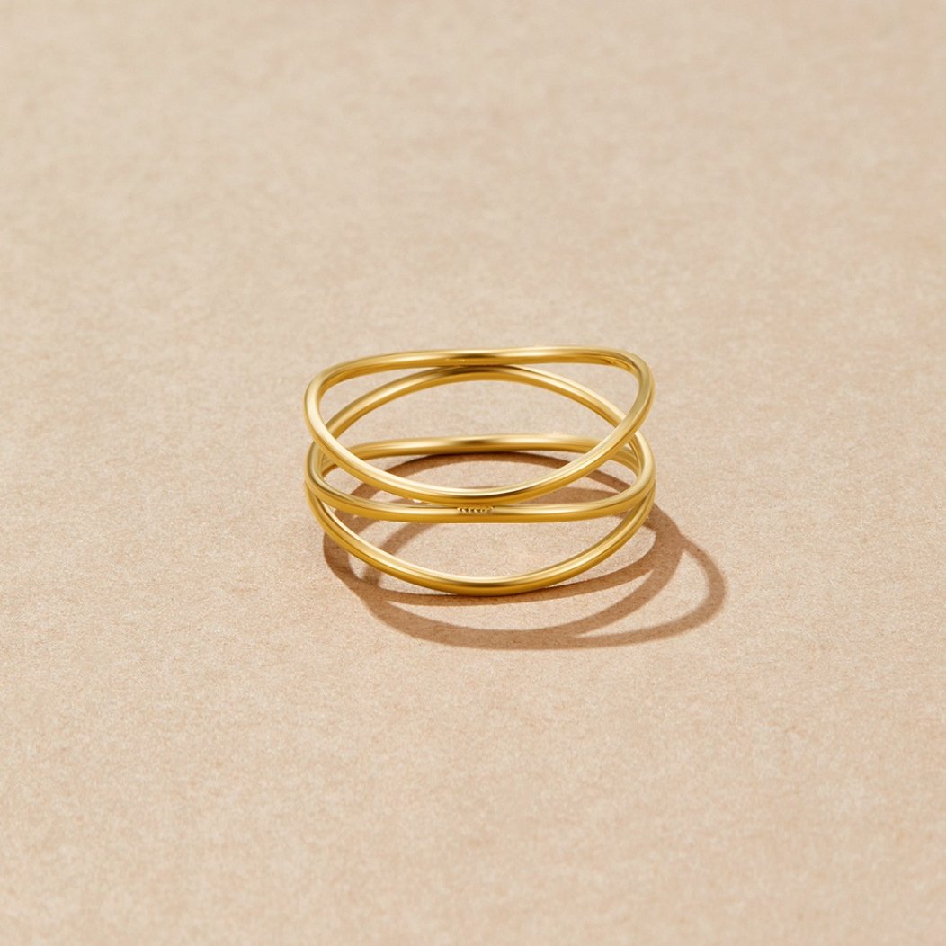 Gold Infinity Loop Ring, gold ring with crossed interlocking bands on a beige surface