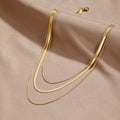 Gold Multi-Layered Chain Necklace, three gold chains layered on beige fabric, lobster clasp at