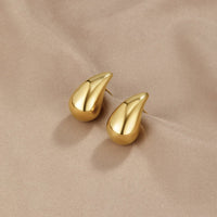 Amara Gold Teardrop Earrings, pair of polished gold teardrop earrings lying on beige satin