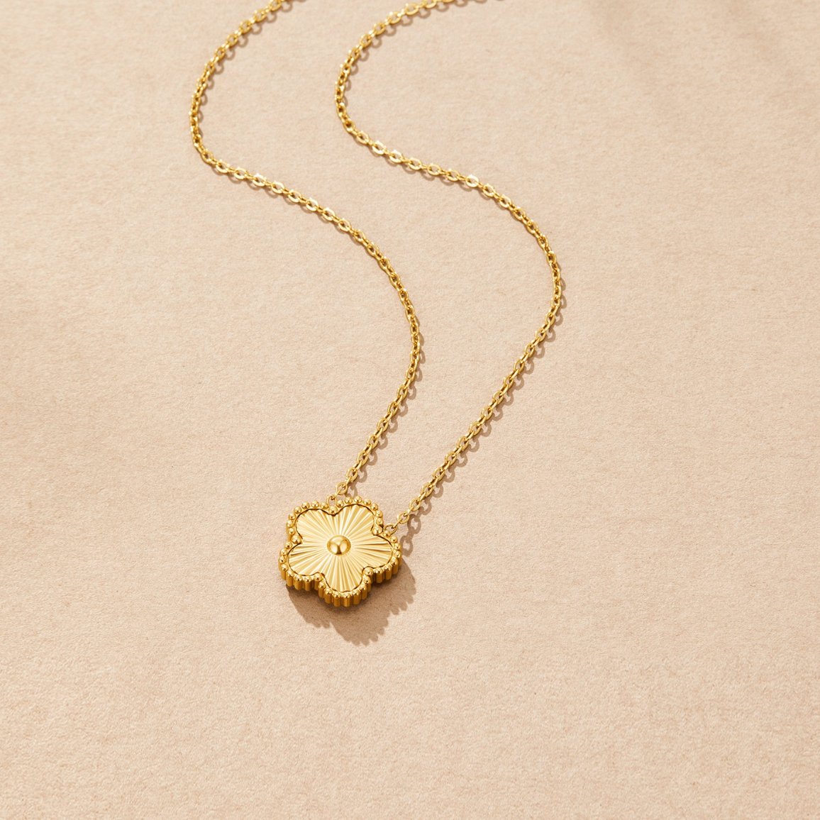 Golden Clover Necklace, lying flat on beige suede, gold clover pendant on fine chain
