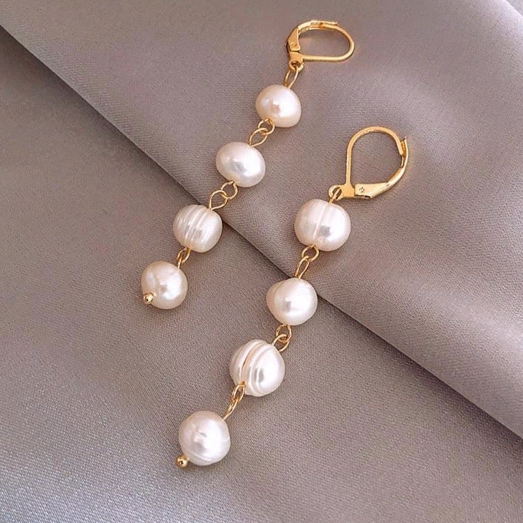 Golden Freshwater Pearl Earrings, a pair of drop earrings laid on grey satin, gold hooks and pearls
