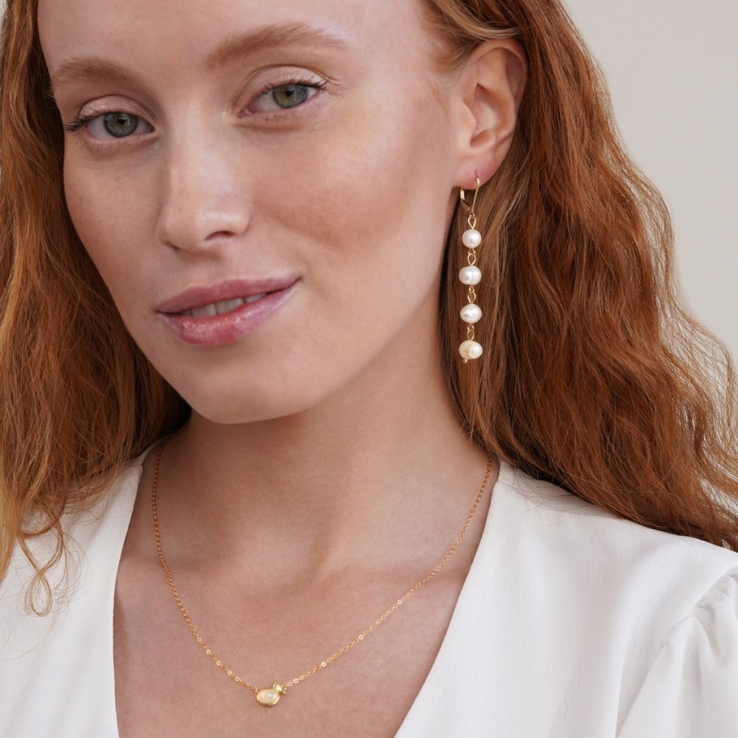 Golden Freshwater Pearl Earrings, worn by a model with a white top and gold necklace