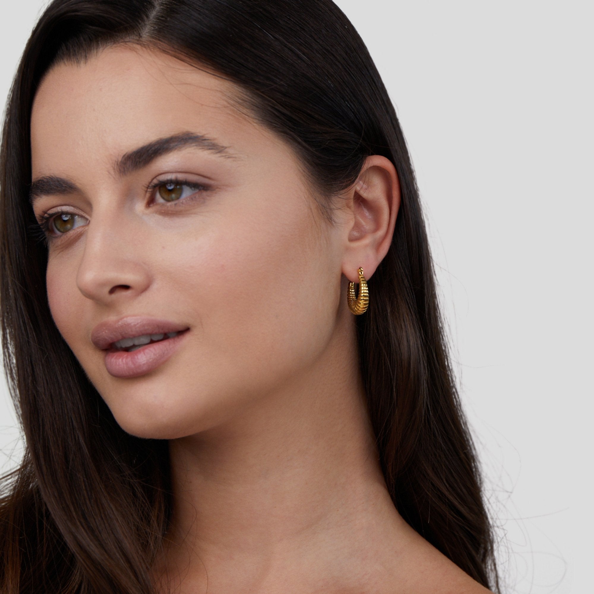 Golden Mia Croissant Hoop Earrings, worn in one ear on a model with long dark hair