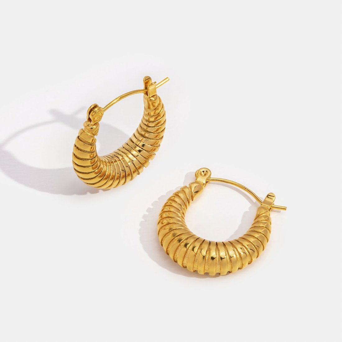 Golden Mia Croissant Hoop Earrings, pair of ribbed gold hoops lying on white surface