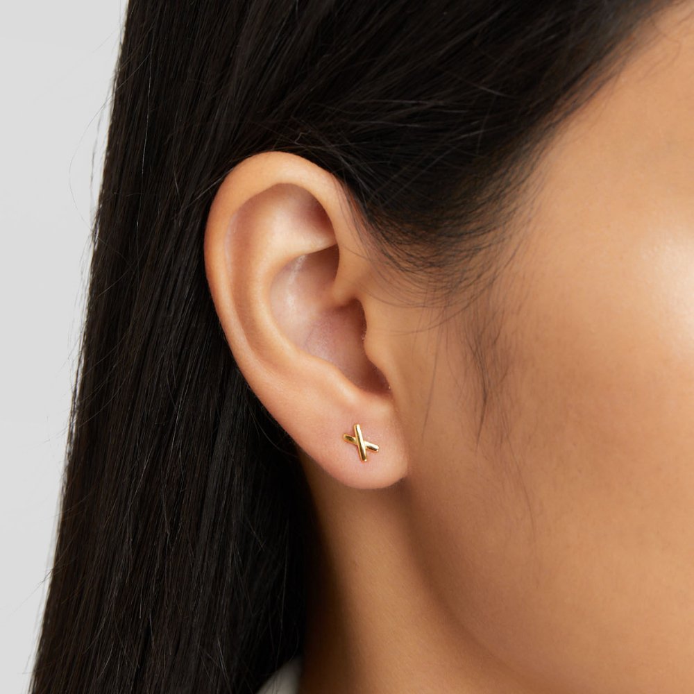 Graffiti X Stud Earrings, worn in an ear, small gold cross-shaped stud