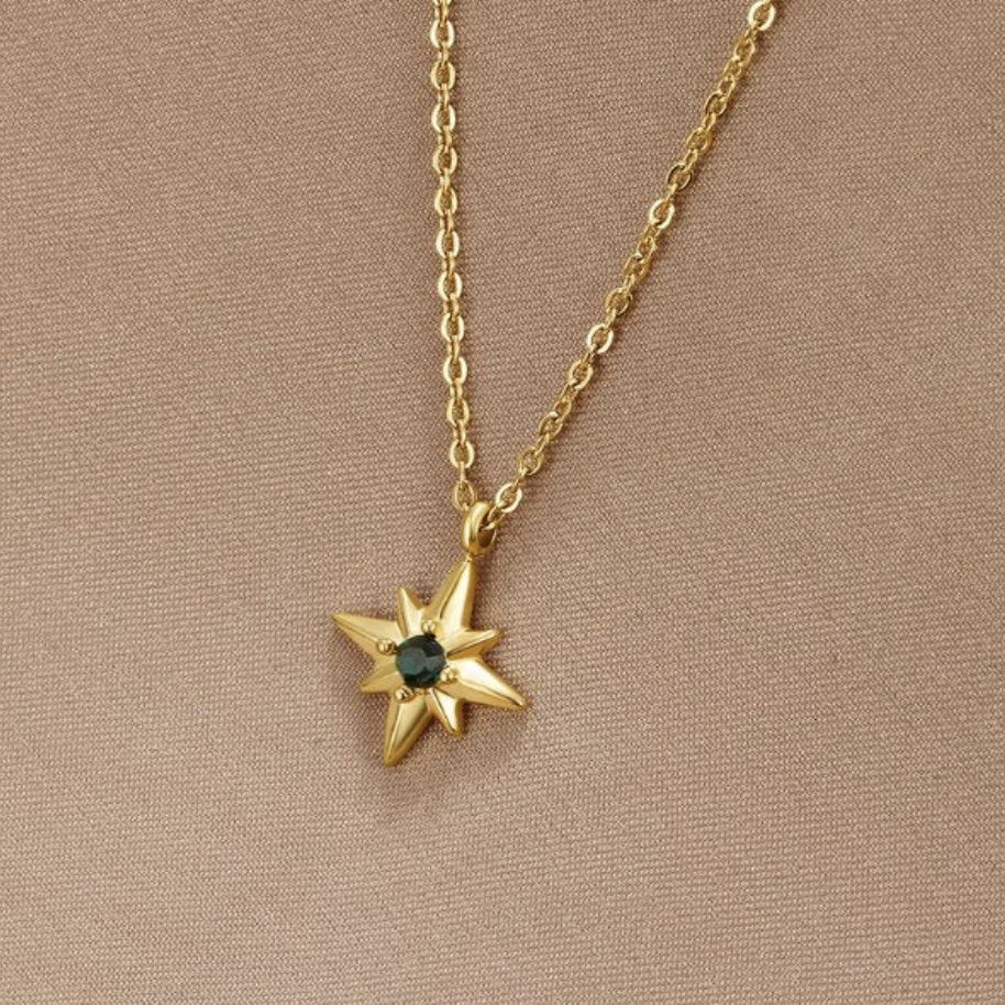 Guiding Star Emerald Crystal Necklace, worn on a beige fabric backdrop, gold chain with star
